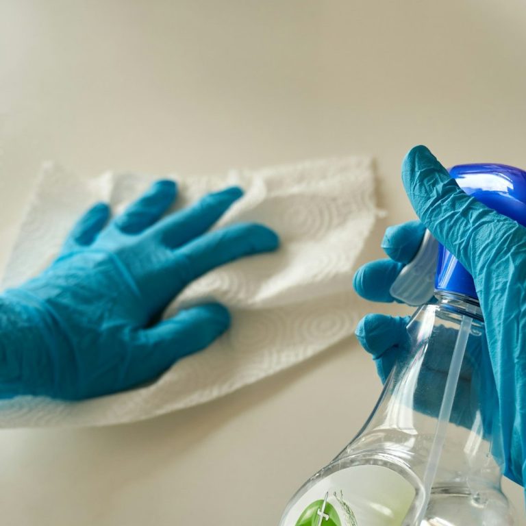 Eine behandschuhte Hand reinigt mit Spray eine Oberfläche- steht für moderne, gründliche Reinigungstechniken.