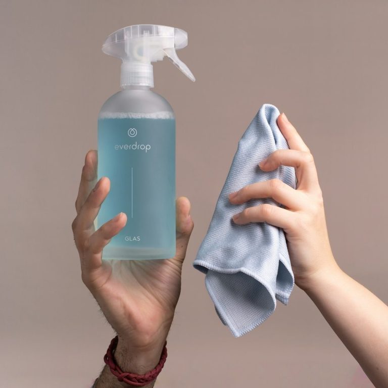 Zwei Hände halten eine blaue Sprayflasche und ein Reinigungstuch- Symbol für umweltschonende Reinigungsmittel.